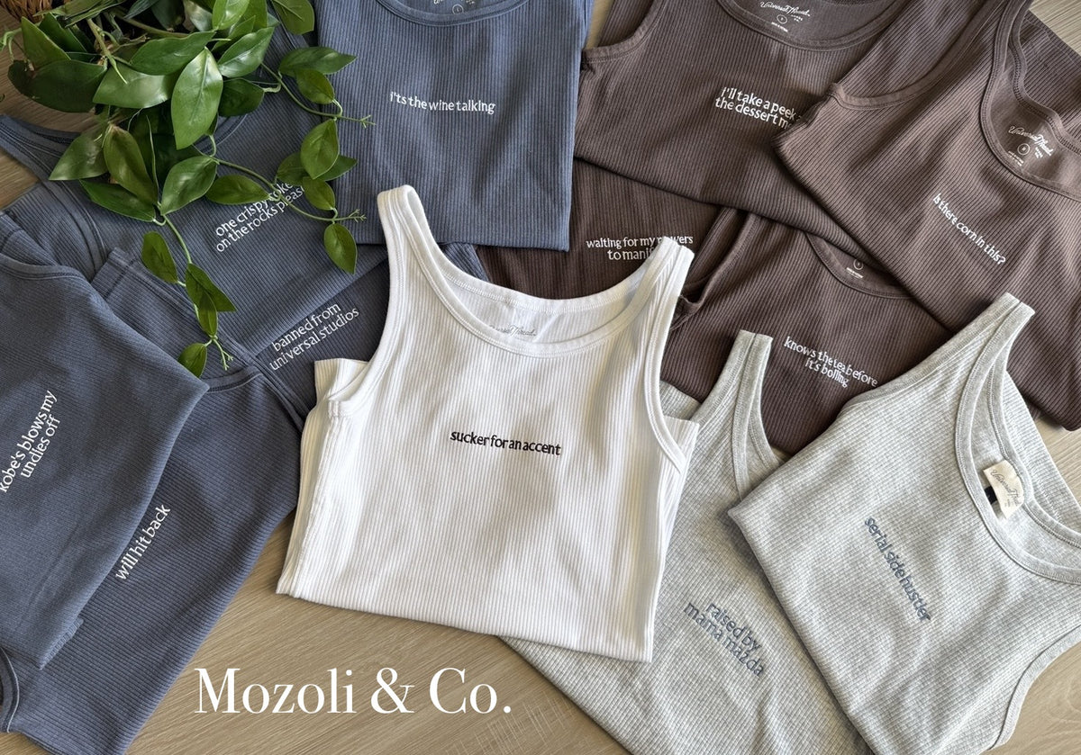Mozoli & Co. personalized ribbed tanks in white, grey, blue and brown, each with a short custom saying in small centered lettering