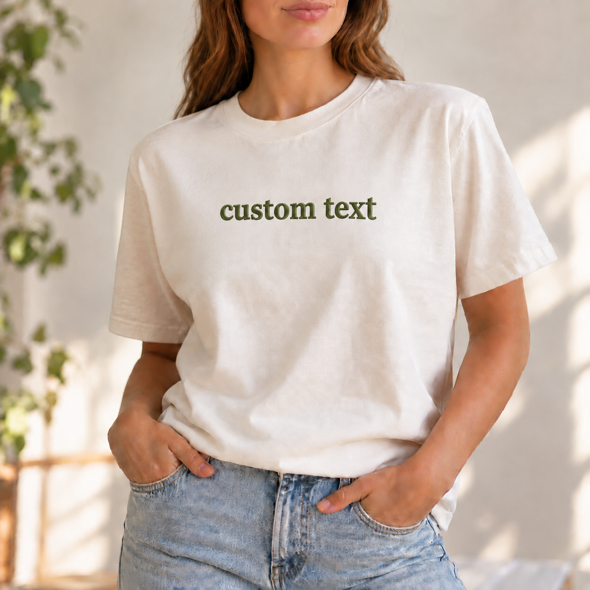 Sample: ivory tee with “custom text” embroidered in olive thread, centered on the chest